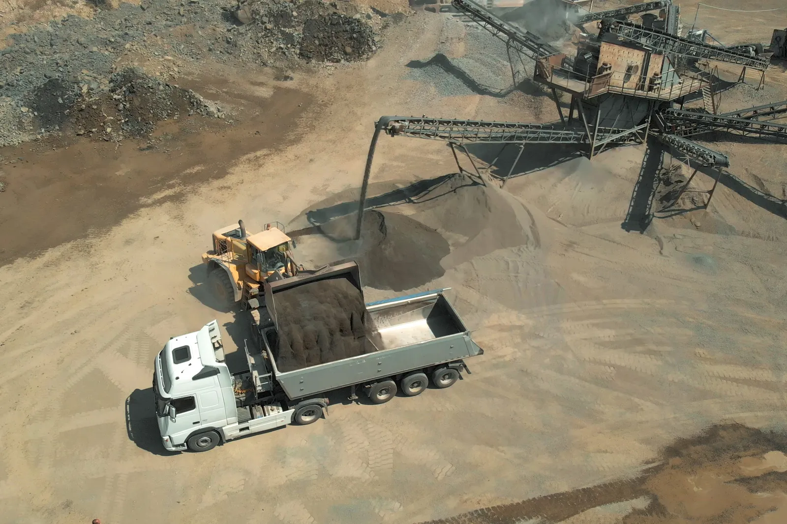 A wheel loader filling a tipper truck at a crushing plant while the cycle waits on the loading unit